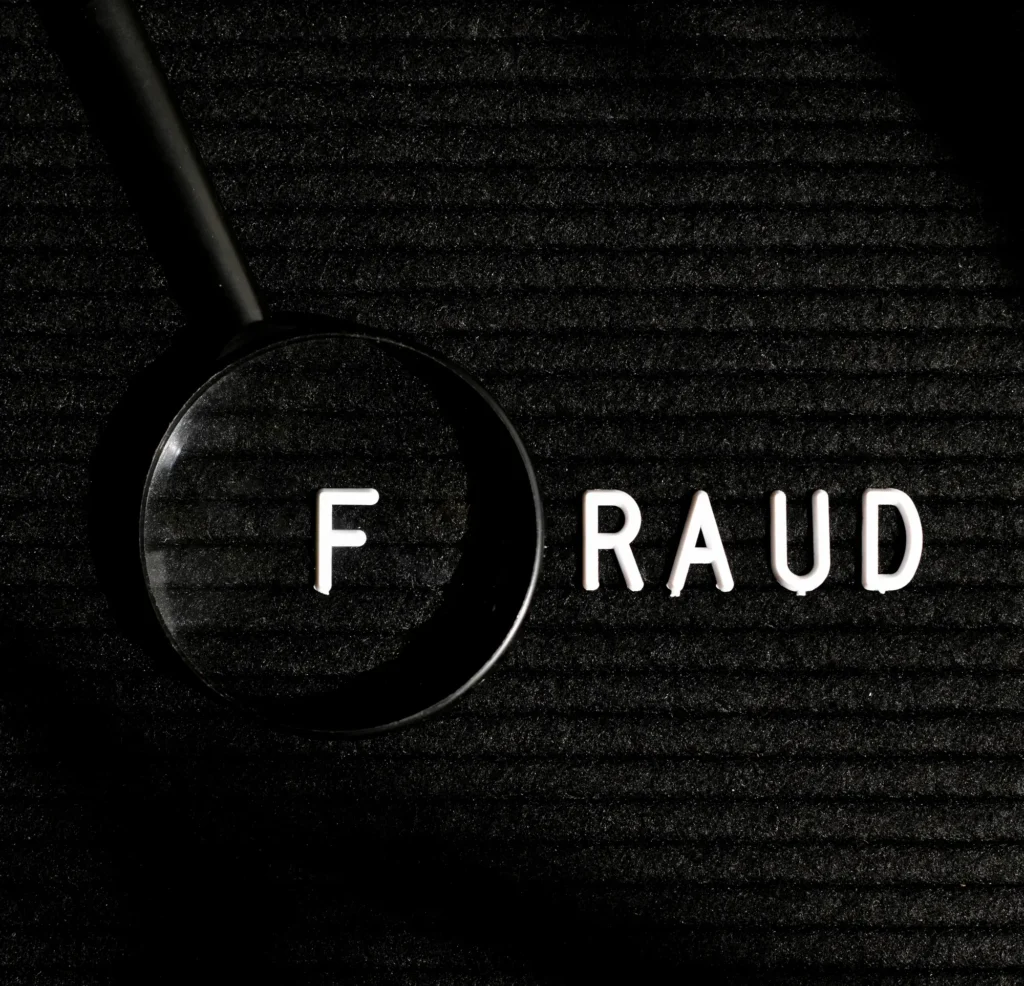 Magnifying glass highlighting word fraud on dark background