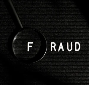 Magnifying glass highlighting word fraud on dark background